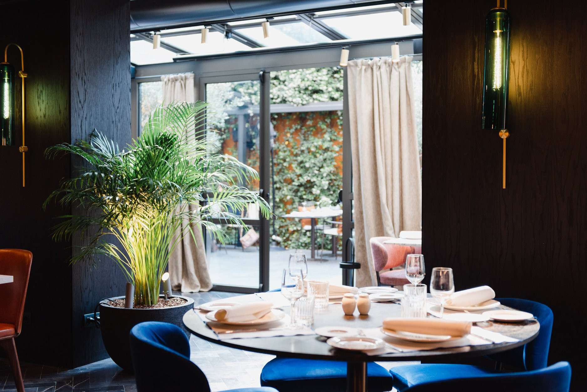 Terraza de restaurante con jardineras, plantas colgantes y jardines verticales que crean un ambiente acogedor y verde para los comensales